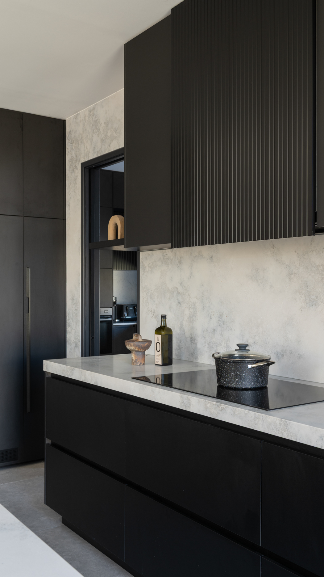 Floor to ceiling stone splashback behind an induction cooktop with black fluted overhead cabinets