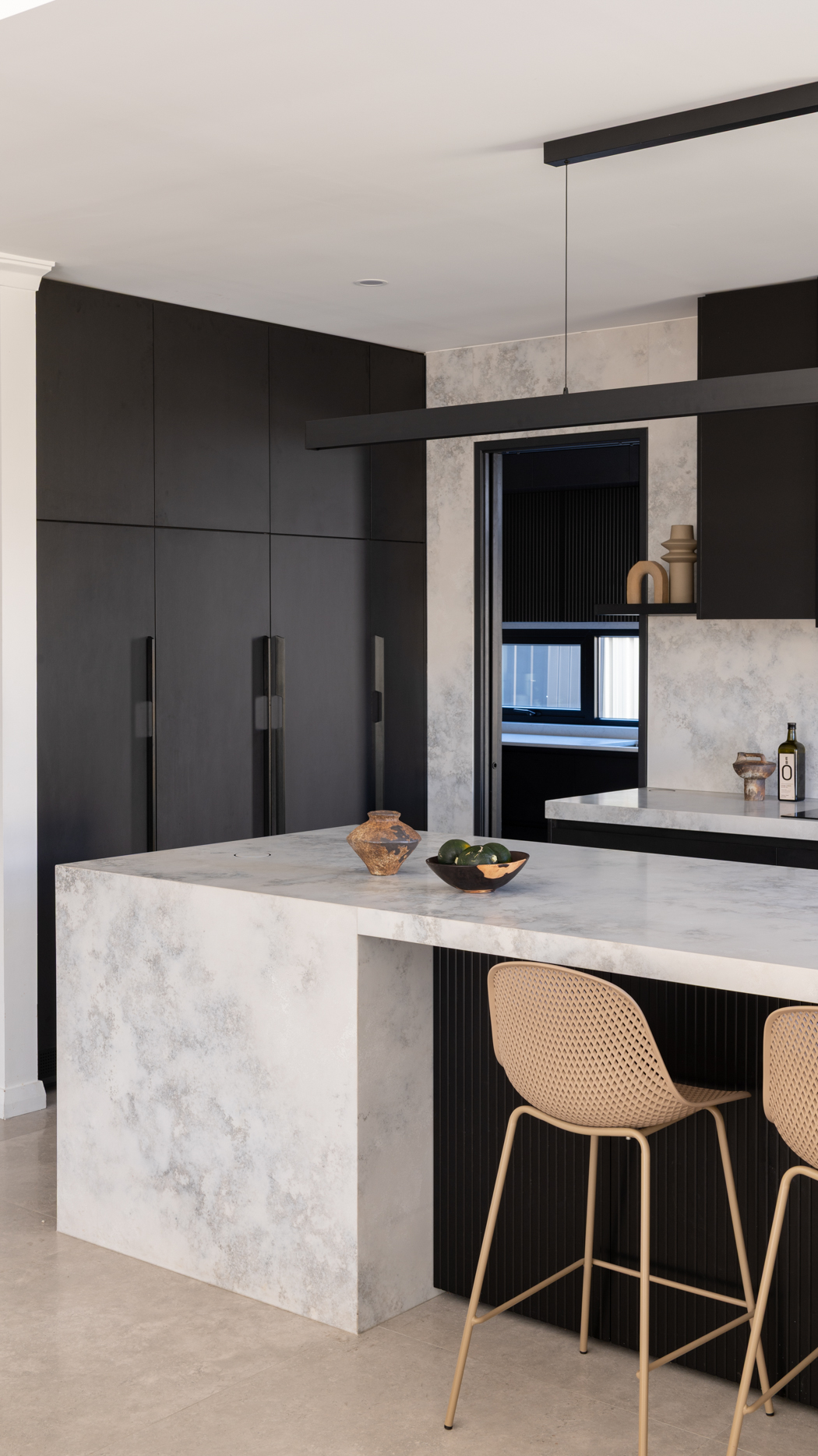 Stone waterfall island with black cabinetry and full height stone splashback