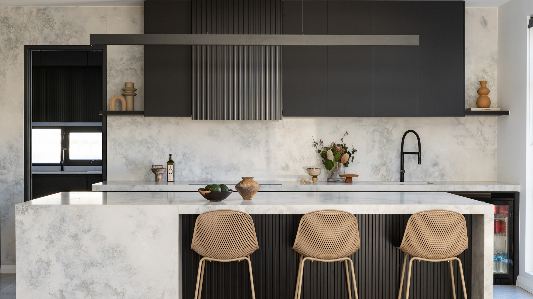 Floor to ceiling stone splashback with black fluted cabinetry and stone waterfall island in a Burns Beach kitchen